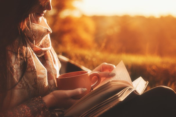 Beautiful girl in autumn forest reading a book covered with a warm blanket.a woman sits near a tree in an autumn forest and holds a book and. Girl reading a book