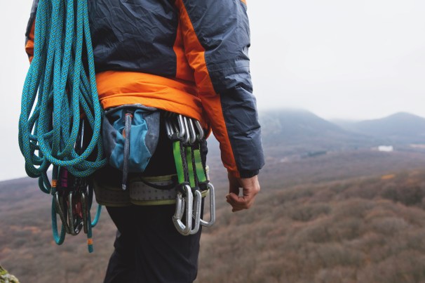 Close-up of a thigh climber with equipment on a belt stands on a rock.jpg