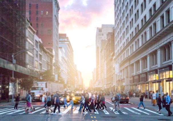 Crowds of diverse people cross the busy intersection on 23rd Street and 5th Avenue in Manhattan with rush hour traffic in the background