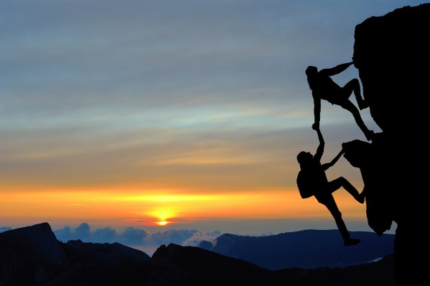 The joint work teamwork of two men travelers help each other on top of a mountain climbing team a beautiful sunset landscape